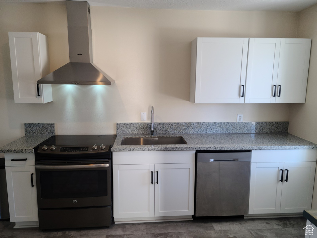 Kitchen featuring stainless steel appliances, wall chimney exhaust hood, a sink, and white cabinets