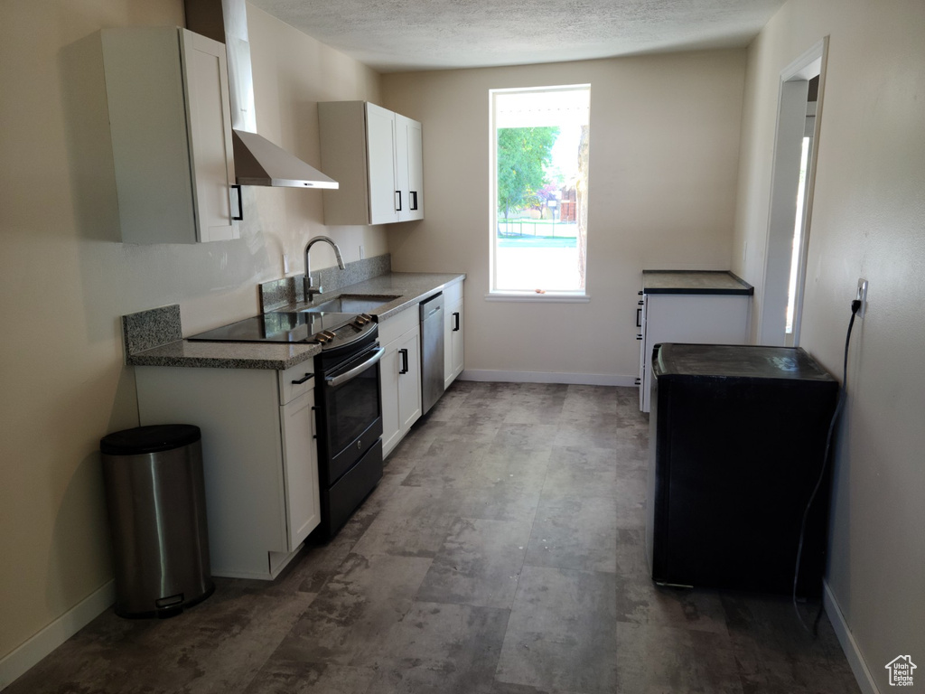 Kitchen with range with electric cooktop, a sink, stainless steel dishwasher, white cabinets, and wall chimney exhaust hood