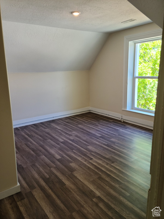 Additional living space featuring vaulted ceiling, a textured ceiling, dark wood-type flooring, and baseboards
