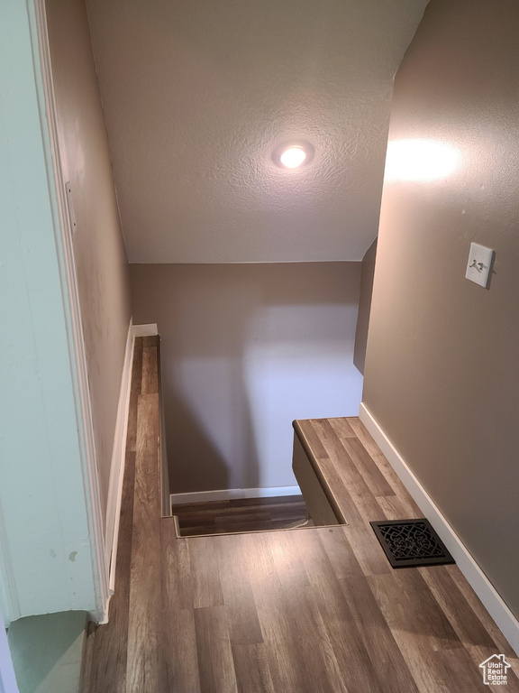 Stairs with wood finished floors, a textured ceiling, and baseboards