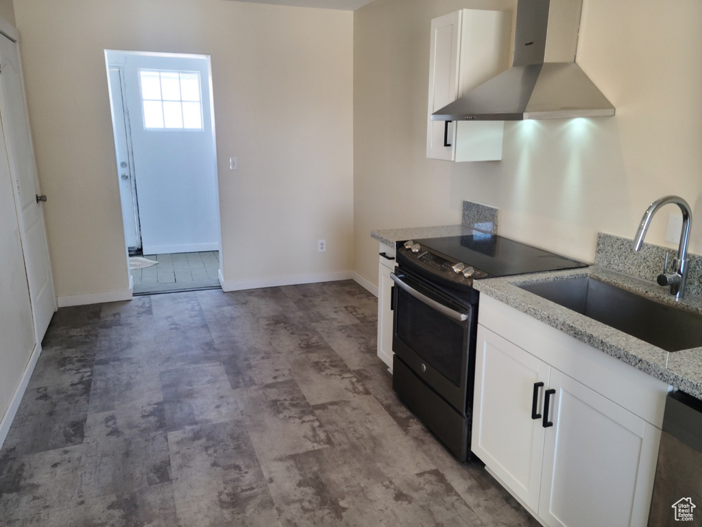 Kitchen with wall chimney range hood, electric stove, a sink, white cabinets, and baseboards