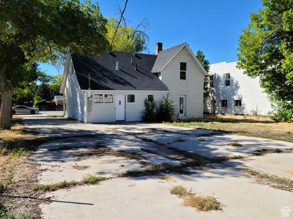 View of side of home featuring concrete driveway, a chimney, and roof with shingles
