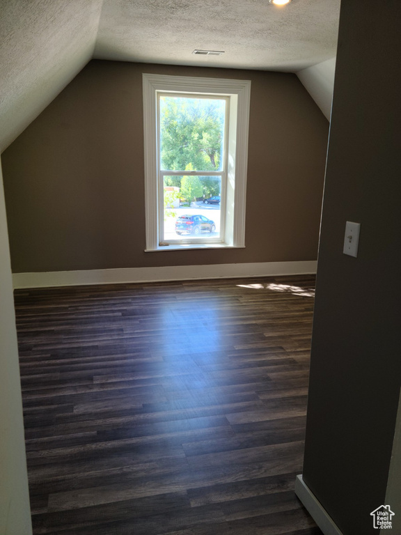 Bonus room with a textured ceiling, lofted ceiling, dark wood-type flooring, and baseboards