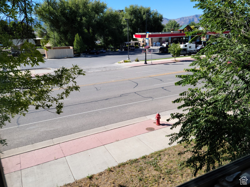 View of asphalt road featuring sidewalks, curbs, street lighting, and a mountain view