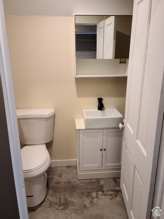 Bathroom with vanity, toilet, baseboards, and concrete flooring