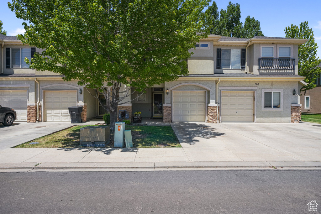 Multi unit property featuring stucco siding, driveway, stone siding, and an attached garage