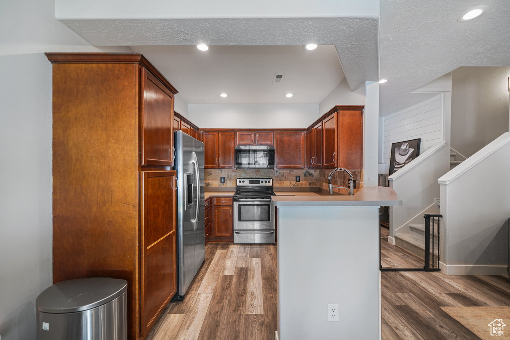 Kitchen with appliances with stainless steel finishes, a peninsula, light wood-style floors, light countertops, and decorative backsplash