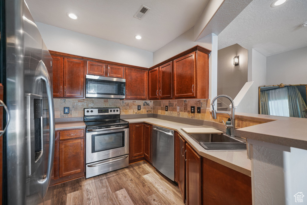 Kitchen with appliances with stainless steel finishes, light wood-style floors, decorative backsplash, light countertops, and a peninsula