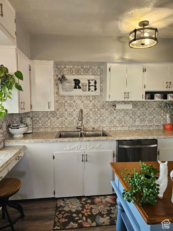 Kitchen with stainless steel dishwasher, dark wood-type flooring, backsplash, and white cabinetry