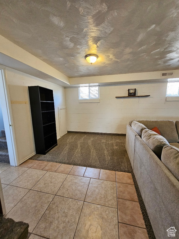 Living area with a textured ceiling, light carpet, light tile patterned floors, and concrete block wall
