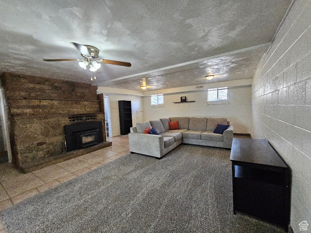 Tiled living room featuring concrete block wall, a textured ceiling, a large fireplace, and ceiling fan