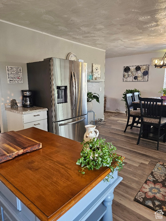 Kitchen with stainless steel refrigerator with ice dispenser, a chandelier, dark wood-style flooring, white cabinets, and a textured ceiling