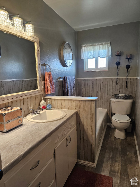 Full bath featuring wainscoting, wood-type flooring, a tub to relax in, vanity, and wood walls