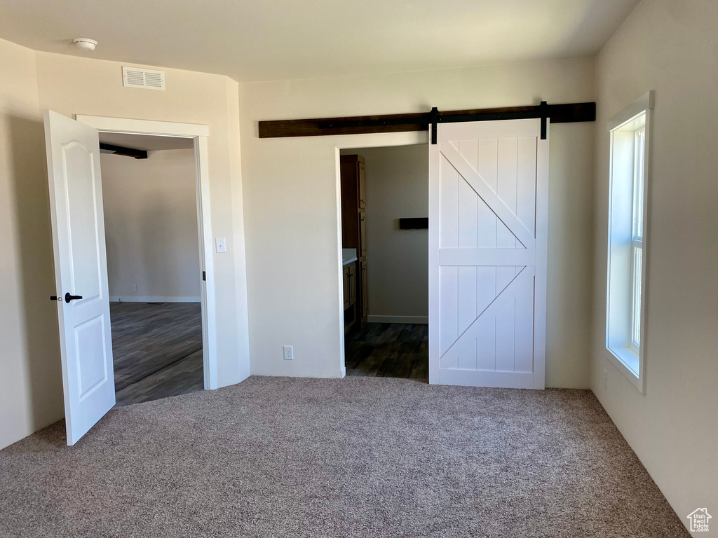 Unfurnished bedroom featuring carpet floors and a barn door