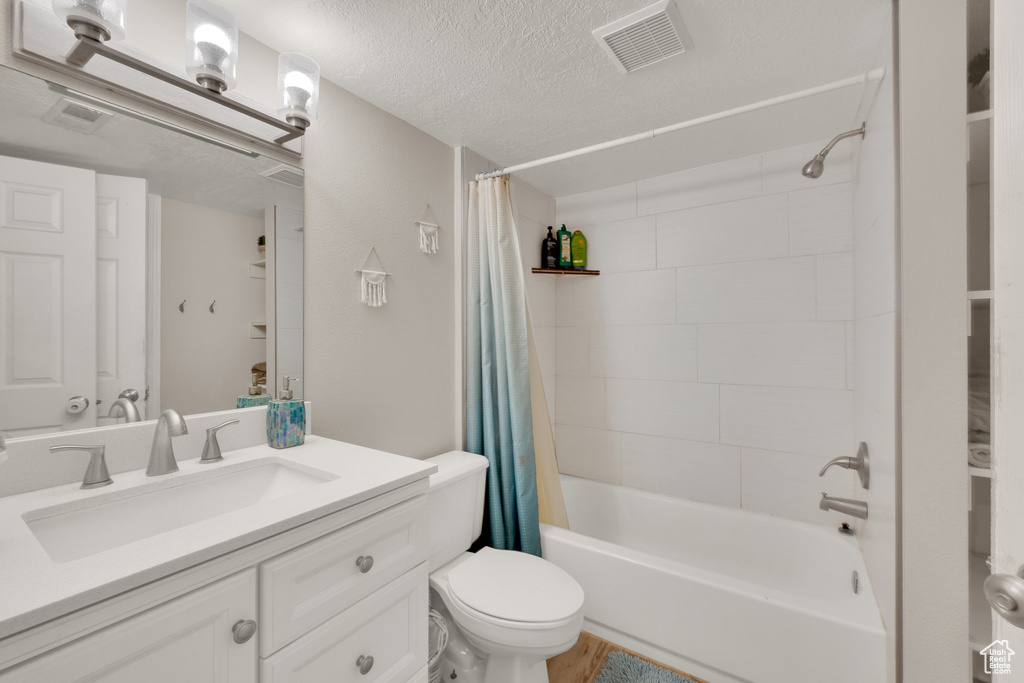 Full bath featuring shower / bath combo with shower curtain, vanity, and a textured ceiling