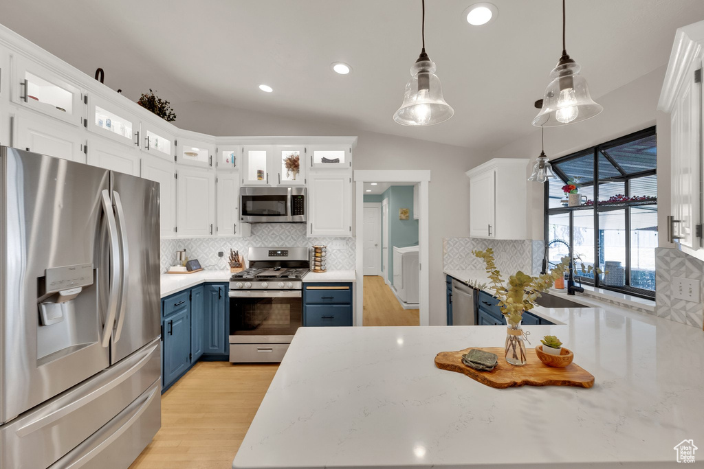 Kitchen featuring stainless steel appliances, blue cabinets, white cabinets, decorative backsplash, and lofted ceiling