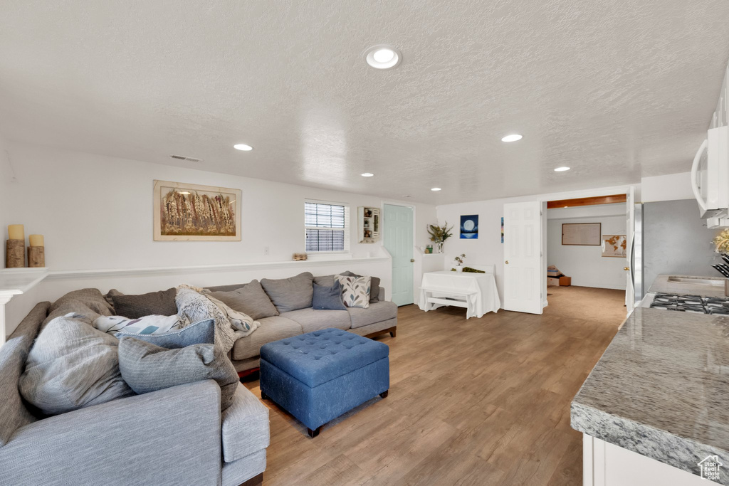 Living area with light wood finished floors, a textured ceiling, and recessed lighting