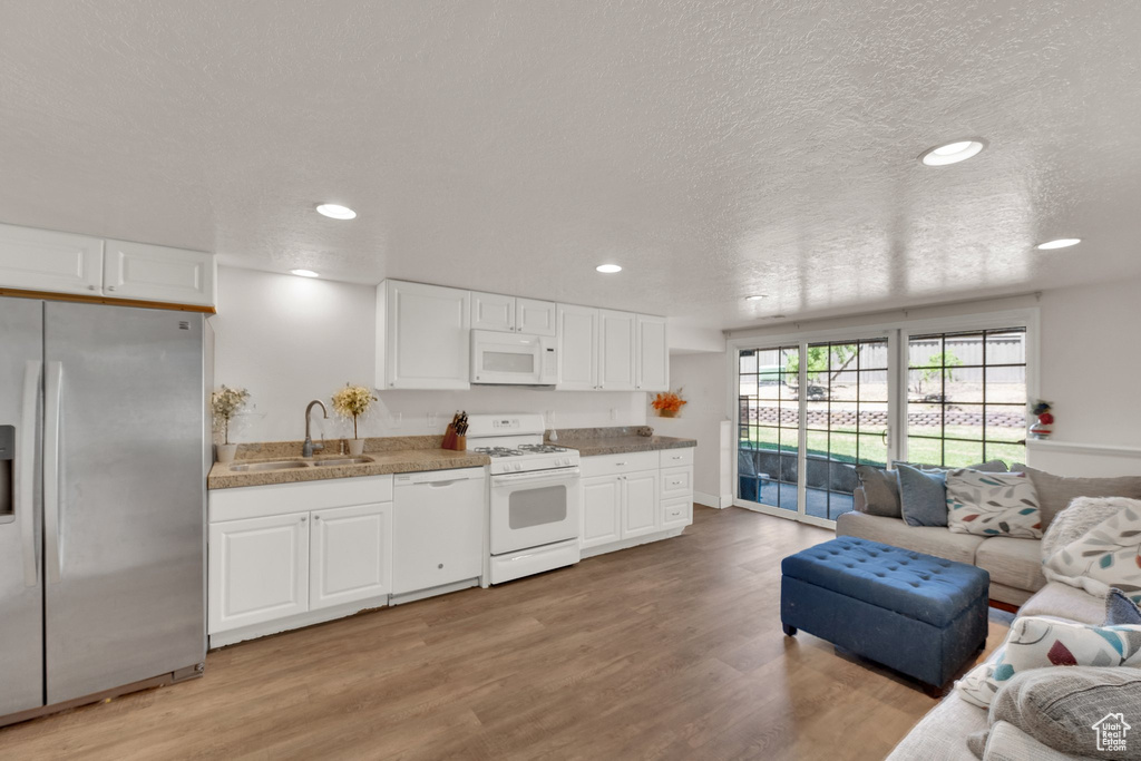Kitchen with white appliances, open floor plan, white cabinets, recessed lighting, and a textured ceiling