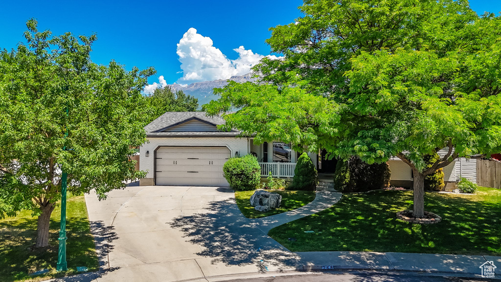 Obstructed view of property featuring concrete driveway, a garage, a front lawn, a mountain view, and brick siding