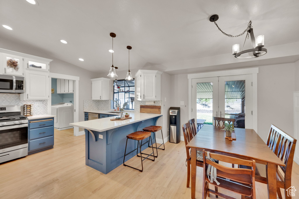 Kitchen with appliances with stainless steel finishes, washing machine and clothes dryer, tasteful backsplash, white cabinets, and a kitchen breakfast bar