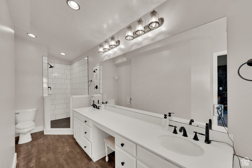Full bath with a tile shower, double vanity, recessed lighting, and wood finished floors