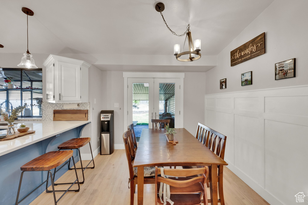 Dining area featuring a chandelier, light wood-style floors, french doors, and a wainscoted wall