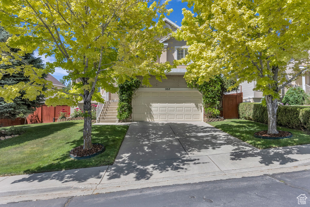 View of property hidden behind natural elements with stairway, concrete driveway, and an attached garage