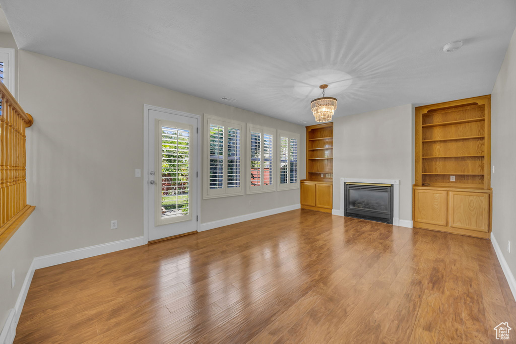 Unfurnished living room with built in shelves, wood finished floors, a glass covered fireplace, and a chandelier