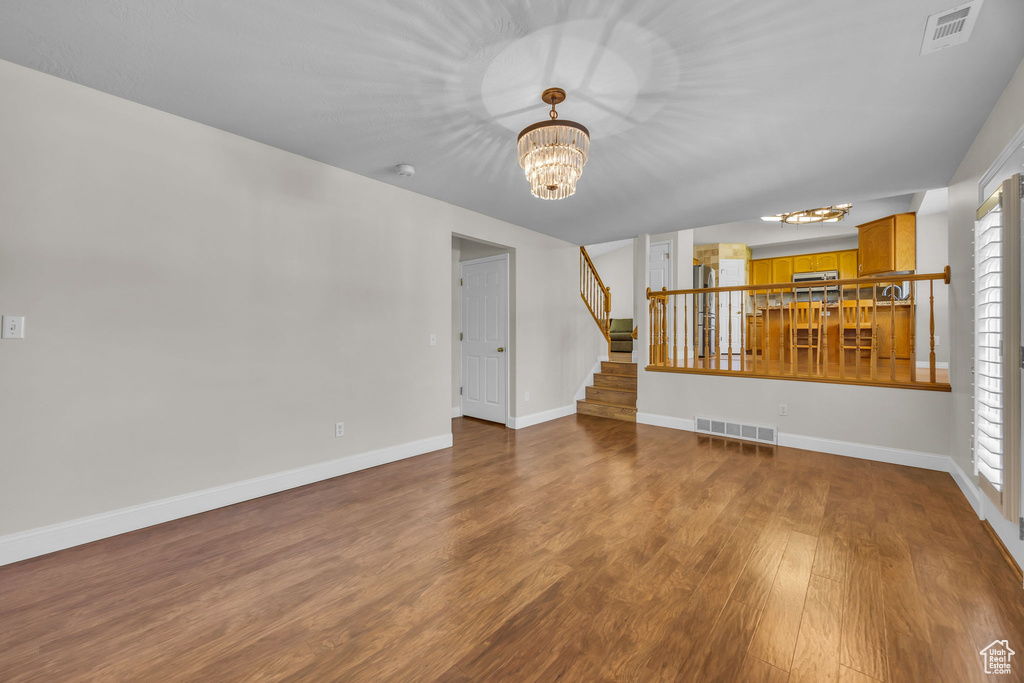 Unfurnished living room with a chandelier, stairs, wood finished floors, and plenty of natural light