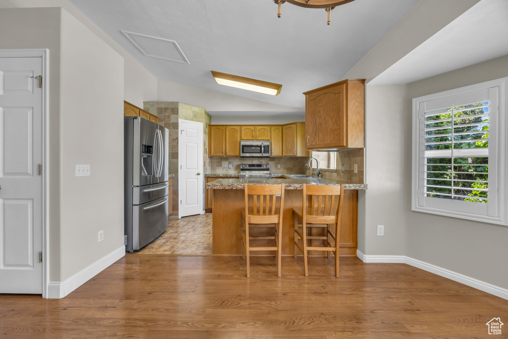 Kitchen featuring stainless steel appliances, a peninsula, lofted ceiling, decorative backsplash, and a breakfast bar area