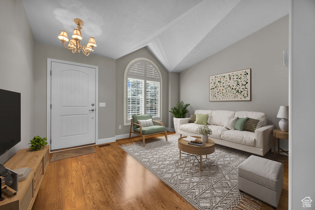 Living room with a chandelier, wood finished floors, and lofted ceiling