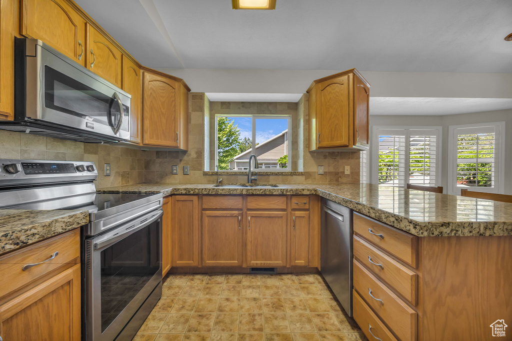 Kitchen featuring stainless steel appliances, a peninsula, decorative backsplash, and brown cabinetry