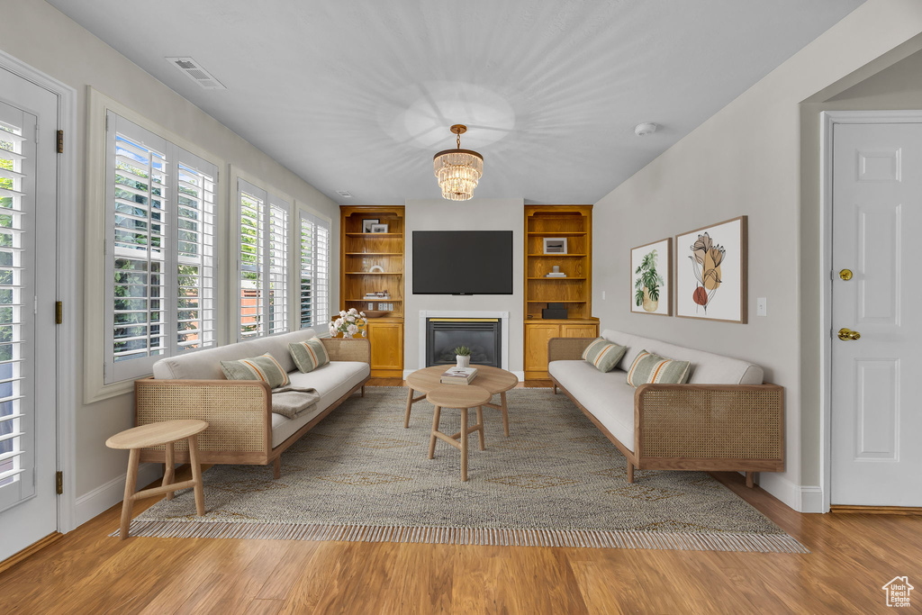 Living room featuring built in features, wood finished floors, a chandelier, and a glass covered fireplace
