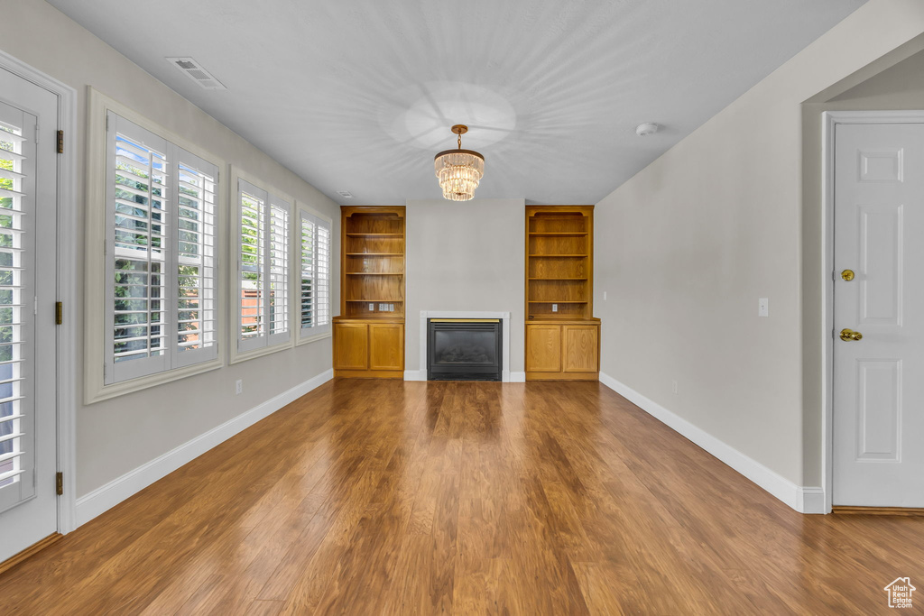 Unfurnished living room with built in shelves, wood finished floors, a glass covered fireplace, and a chandelier