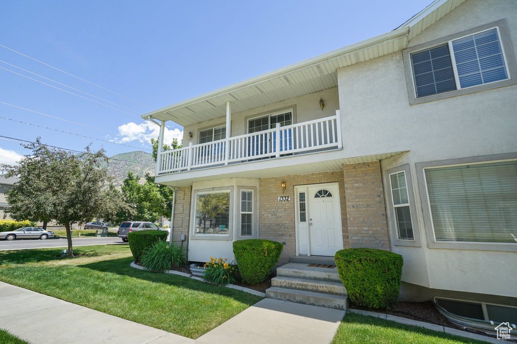 Multi unit property featuring a balcony, a front lawn, stucco siding, and brick siding