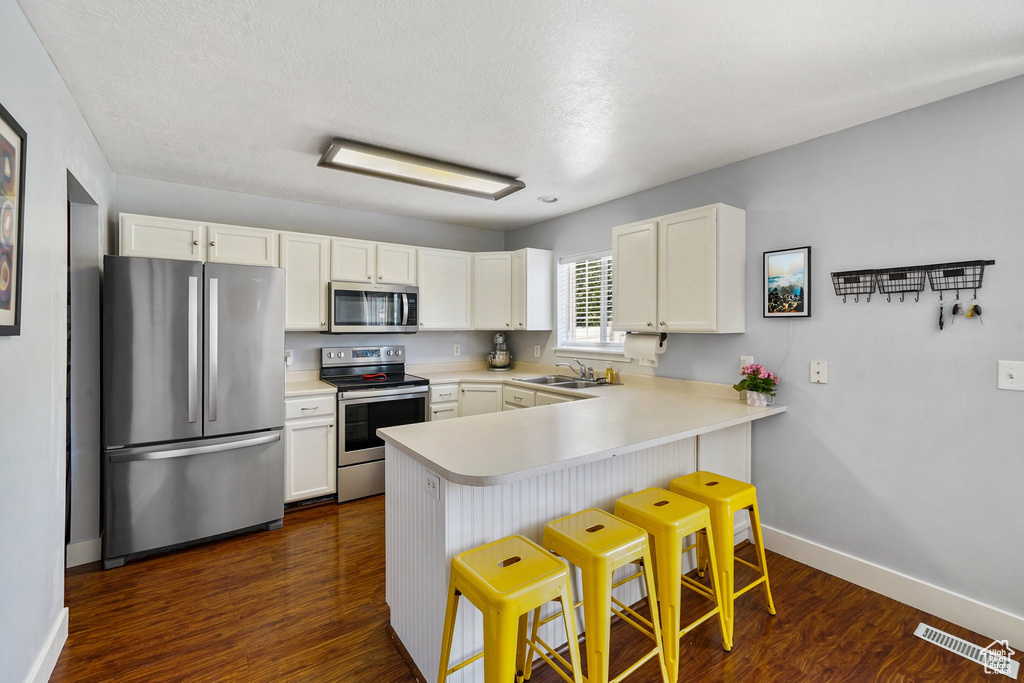 Kitchen featuring appliances with stainless steel finishes, a peninsula, white cabinetry, light countertops, and a kitchen bar