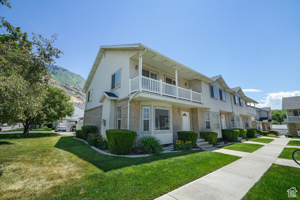 Multi unit property featuring a balcony, a front lawn, stucco siding, a mountain view, and stone siding