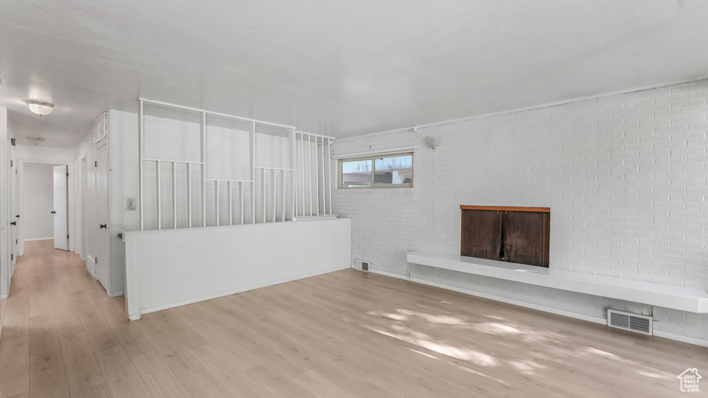 Unfurnished living room with wood finished floors, a fireplace, and brick wall