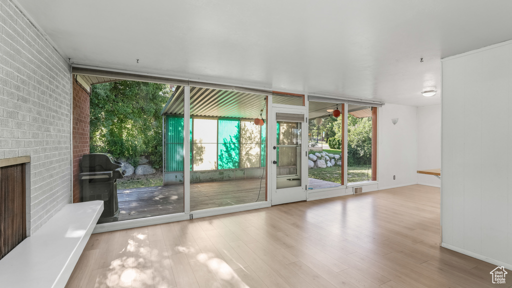 Unfurnished room featuring healthy amount of natural light, wood finished floors, brick wall, baseboards, and a fireplace