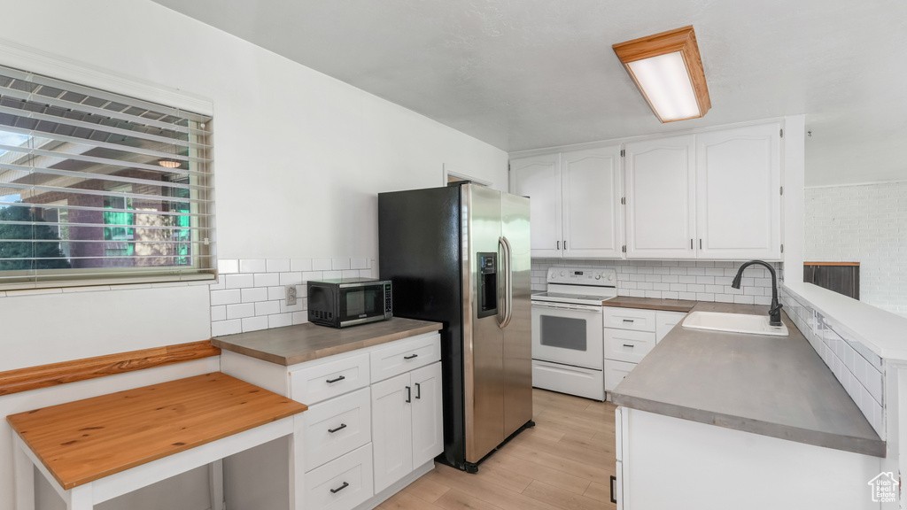 Kitchen with white range with electric cooktop, a sink, light wood-style flooring, stainless steel fridge with ice dispenser, and backsplash