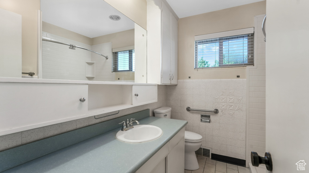 Bathroom with toilet, vanity, tile patterned flooring, tile walls, and a shower
