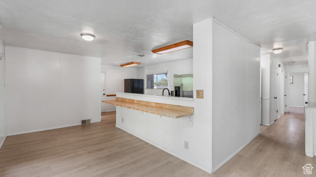 Kitchen with stainless steel fridge with ice dispenser, light wood finished floors, freestanding refrigerator, light countertops, and baseboards