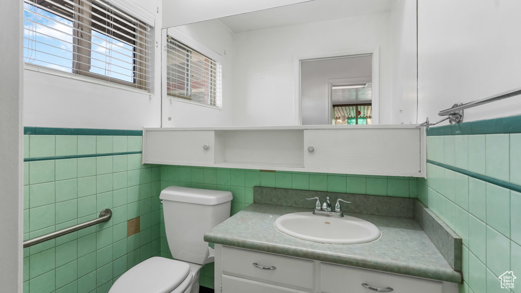 Half bath featuring tile walls, toilet, vanity, and a wainscoted wall