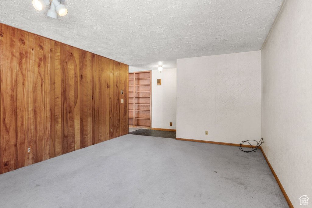 Carpeted empty room featuring a textured ceiling and wood walls