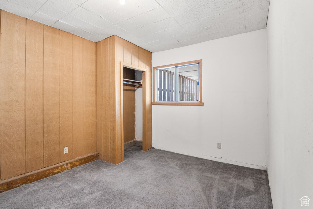 Unfurnished bedroom featuring carpet floors, wood walls, and a closet