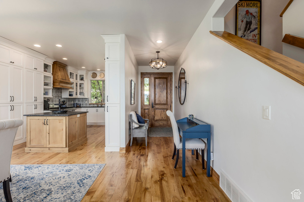 Kitchen featuring light wood-style floors, dark countertops, glass insert cabinets, decorative backsplash, and recessed lighting