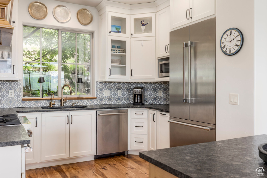 Kitchen featuring appliances with stainless steel finishes, light wood-style floors, white cabinetry, and backsplash