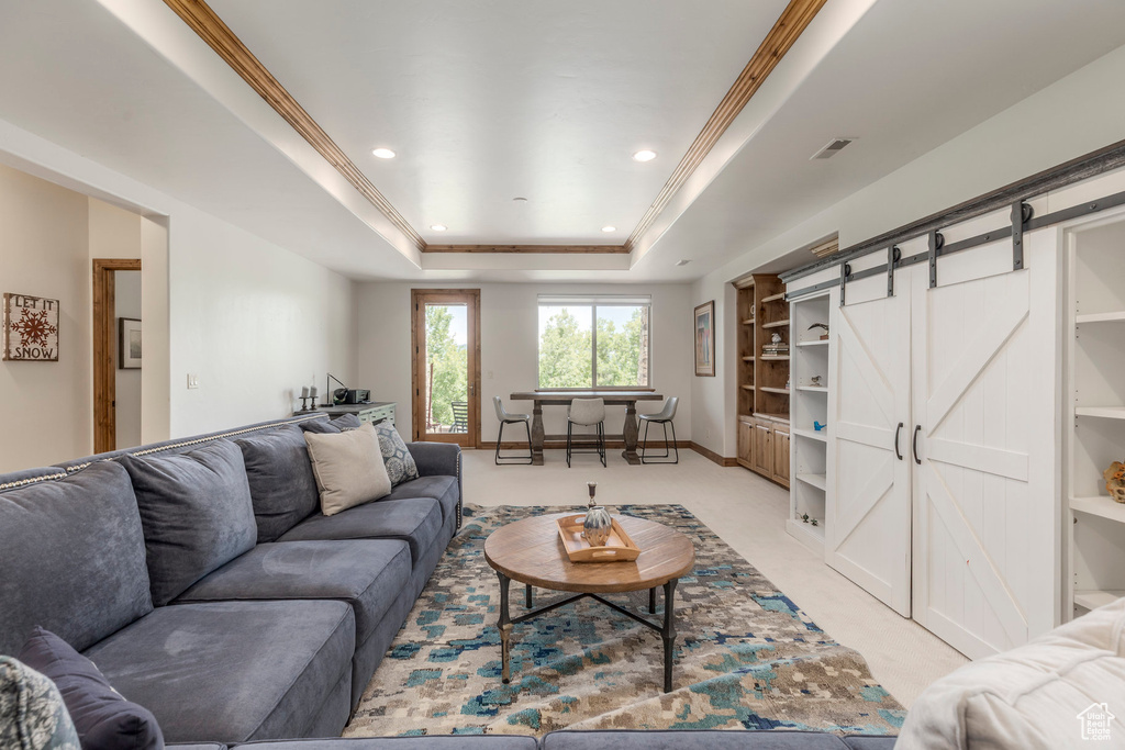 Living area with light colored carpet, a barn door, a raised ceiling, crown molding, and recessed lighting