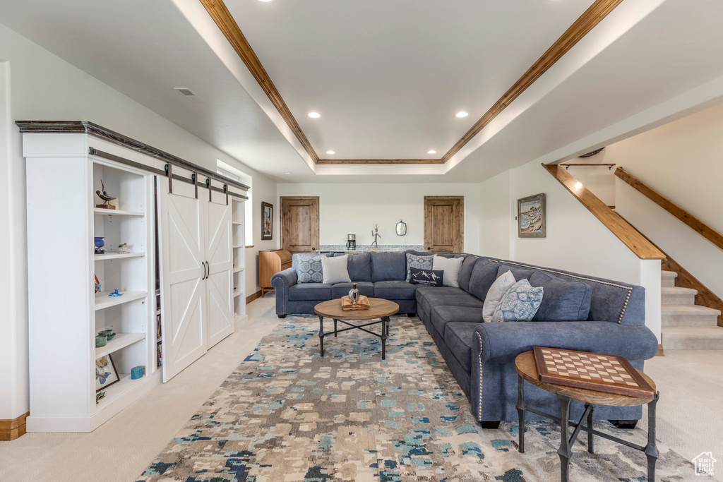 Living room featuring a barn door, recessed lighting, a raised ceiling, crown molding, and stairway