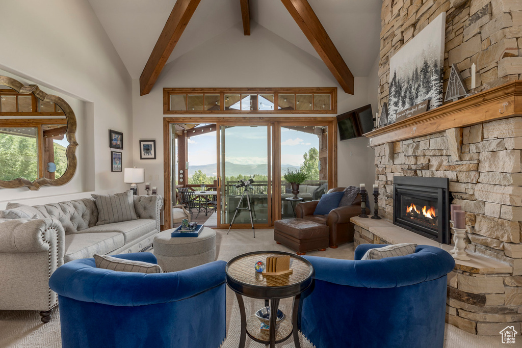 Living room featuring beam ceiling, high vaulted ceiling, a stone fireplace, and carpet